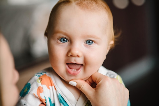 Baby Boy Portrait Blick in die Kamera Closeup Mutter Hände öffnen Baby Mund, um die ersten Zähne zu untersuchen Primärzahn des Säuglings Das glückliche Baby, Säugling mit dem ersten Zahn