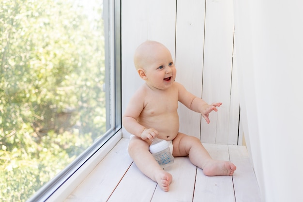 Baby boy sentado en pañales en el alféizar de la ventana