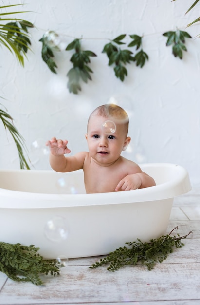 Baby Boy se sienta en un baño blanco y atrapa pompas de jabón