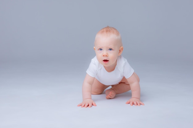 Baby Boy en un traje blanco arrastrándose sobre un fondo blanco.