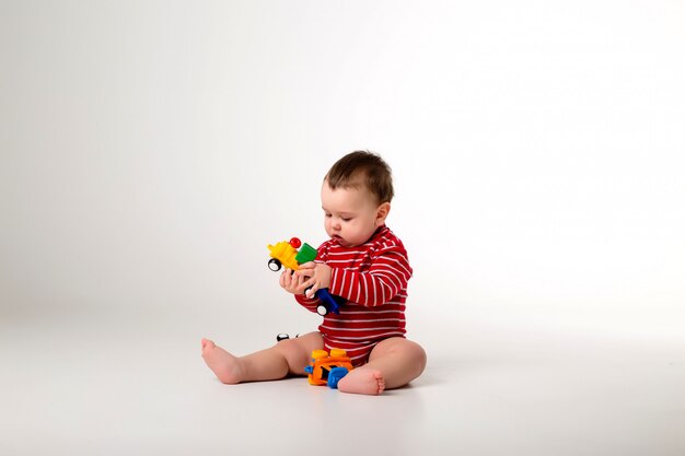 Baby Boy en traje rojo sentado jugando con un juguete en una pared blanca