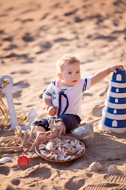 Baby Boy vestido como un marinero en una playa de arena con conchas junto al mar, en una red de pesca