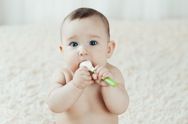 Baby Brust sitzt mit einem Gummilöffel in ihren Händen, die damit spielen