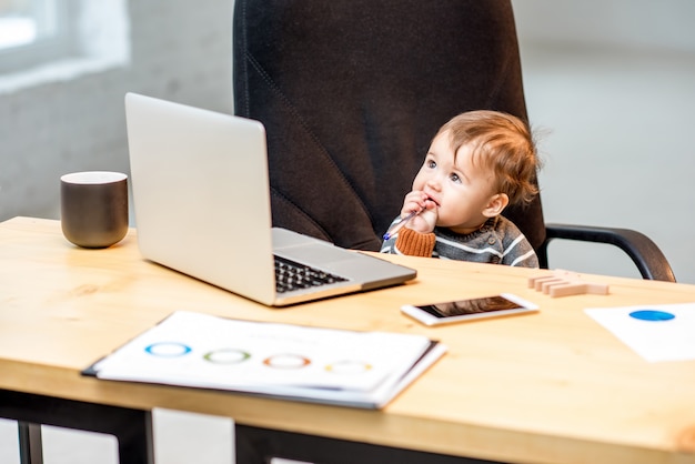 Baby-Chef, der mit Laptop auf dem Stuhl im Büro sitzt