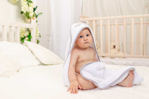 Baby, das auf einem Bett in einem weißen Handtuch sitzt