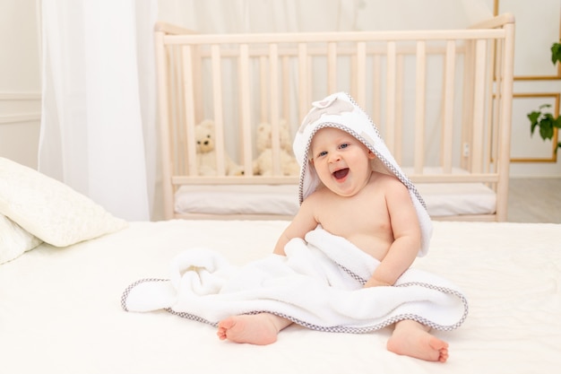 Baby, das auf einem weißen Bett in einem weißen Handtuch sitzt