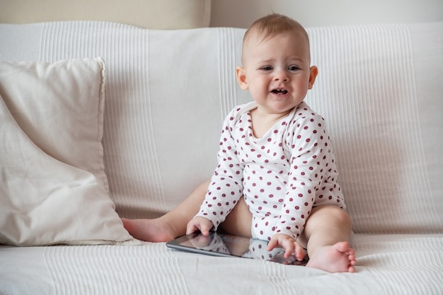 Baby, das auf weißem Sofa sitzt und graue Tablette hält