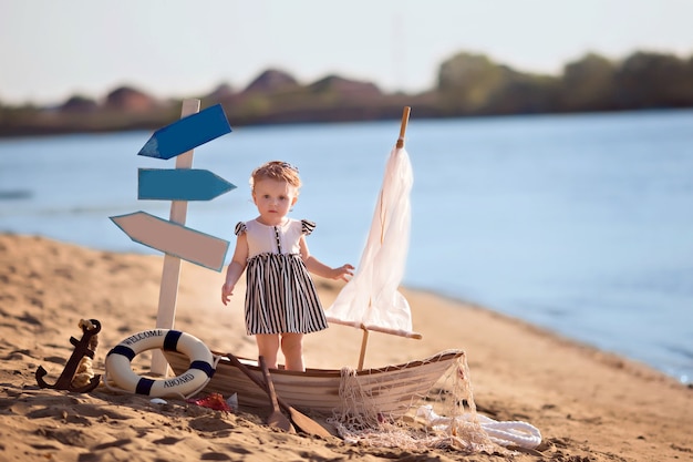 Baby, das in einem Boot sitzt, als Seemann verkleidet, an einem Sandstrand mit Muscheln am Meer