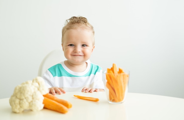 Baby, das in einem Kinderstuhl sitzt und Karottenscheiben auf weißem Hintergrund isst