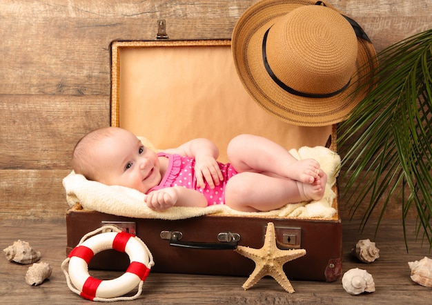 Baby, das in einem Koffer mit Strandzubehör auf braunem Hintergrund liegt