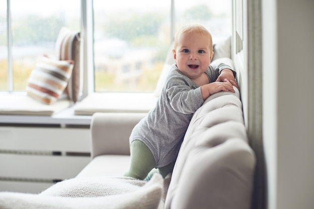 Baby, das kriecht und auf Sofa gegen großes Fenster klettert