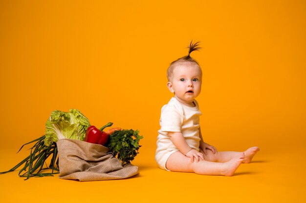 Baby, das mit Beutel des Gemüses auf Orange sitzt