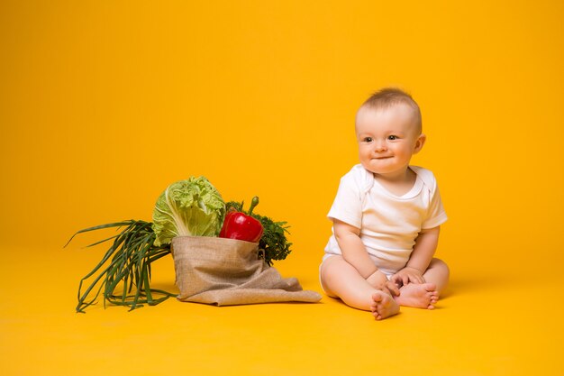 Baby, das mit Tasche des Gemüses auf Gelb sitzt