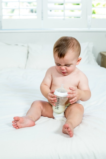 Baby, das zu Hause mit Milchflasche auf Bett sitzt