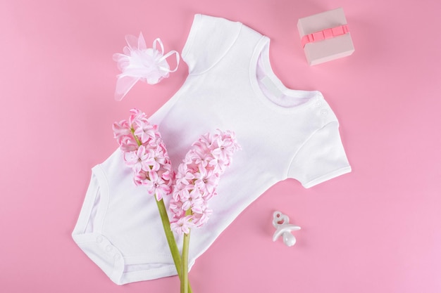 Baby-Dusche-Mockup-Hintergrund, flaches Lay-Kompositions-Layout mit Baby-Girl-Bodysuit, Keramiknippel oder Schnuller des Babys, Geschenkbox und Konfetti und Hyazinthenblumen mit Kopierraum auf rosa Hintergrund