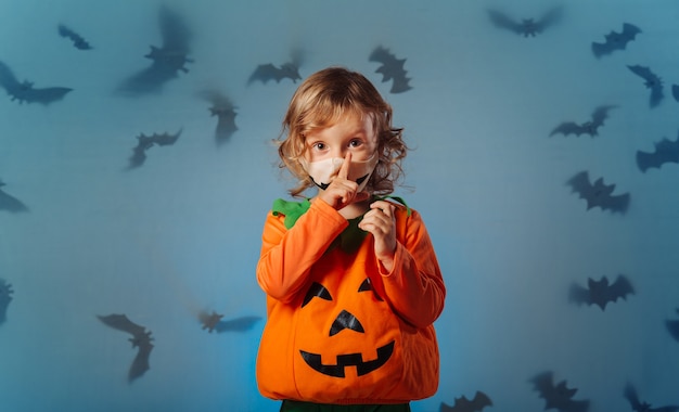 Baby im Karnevalskürbiskostüm, das stilles Zeichen zum Betrachter bei Halloween-Party macht.