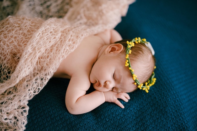 Baby im Kranz mit Schal schläft auf einer blauen Tagesdecke