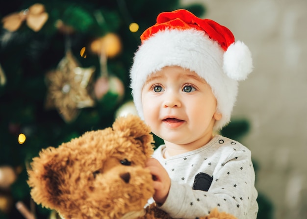 Baby im Weihnachtshut mit Teddybär in den Händen