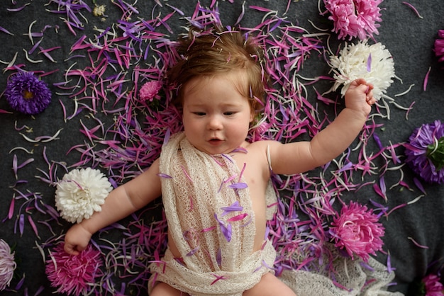 Foto baby im weißen kleid, das mit blumenstrauß spielt