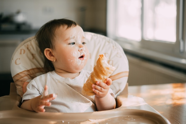 Baby in der Küche isst eifrig die köstlichen Sahnehörner, gefüllt mit einer Vanillecreme