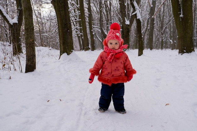 Baby in der roten Jacke, die durch Schnee im Wald geht.