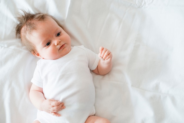 Foto baby in der weißen kleidung, die auf bett legt