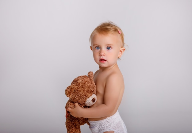 Baby in der Windel, die mit Teddybären spielt, betreffen Weiß