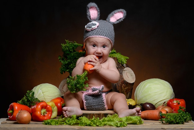 Baby in einem Kaninchenkostüm mit Gemüse auf einem Holz