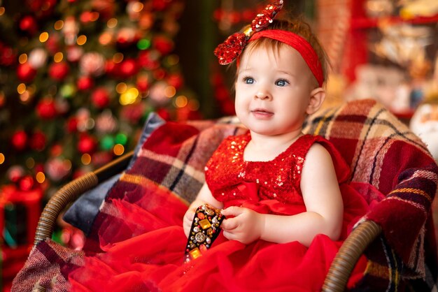 Baby in einem roten Kleid auf dem Hintergrund der Weihnachtsbeleuchtung Weihnachtsporträt