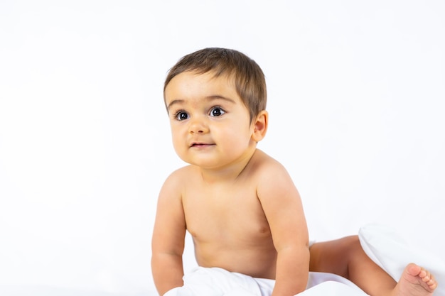 Baby in einem Studio mit weißem Hintergrund, acht Monate altes kaukasisches Neugeborenes, das mit einem Tuch sitzt, spielt und lächelt