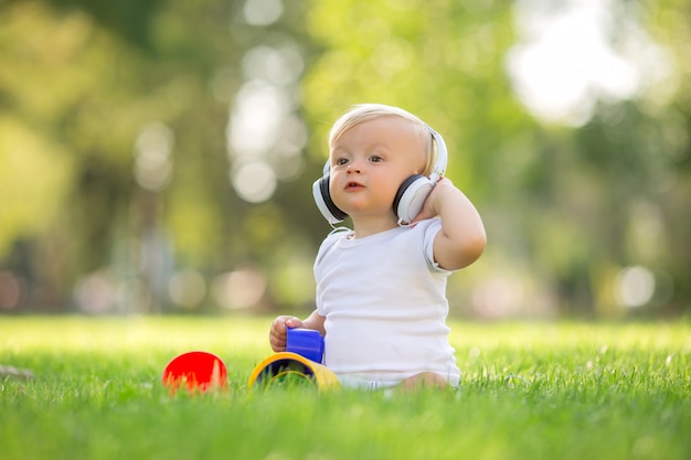 Baby in einem weißen Body, der auf dem Spielen des grünen Grases sitzt