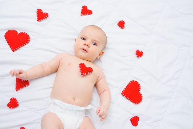 Baby in einer weißen Windel liegt gegen rote Herzen lieben Valentinstag