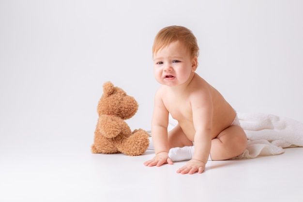 Baby in einer Windel sitzt auf einem weißen Hintergrund mit einem Teddybären