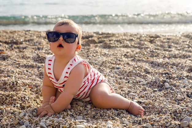 Baby in Hut auf Strandkiesel spielt