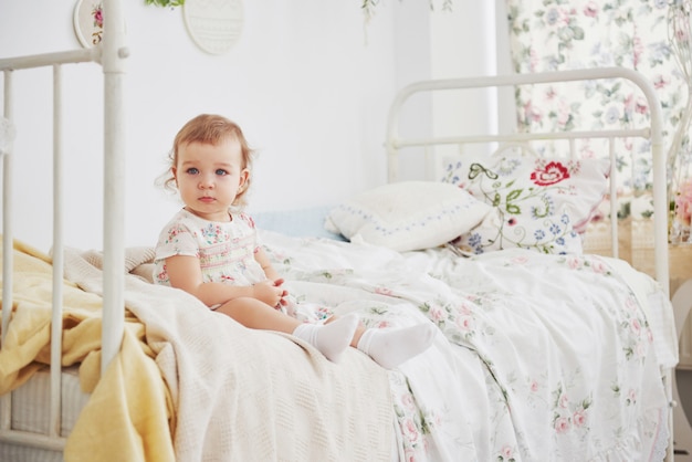 Baby in süßem Kleid, das am Bett durch das Haus sitzt.