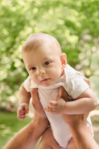 Baby in Vaters Händen füllt nett und zart, Vaterschaft. Netter kleiner Sohn nah oben über grünen Blättern