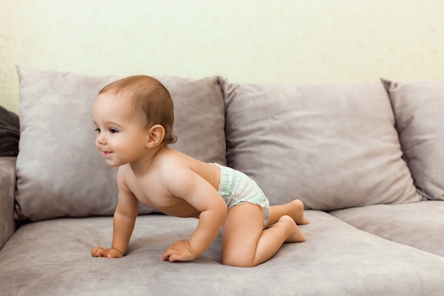 Baby in Windel krabbelt auf der Couch. Baby ist 11 Monate alt.