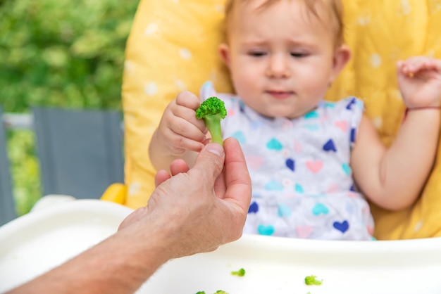 Baby isst Brokkoli-Gemüsestücke. Selektiver Fokus. Kind.