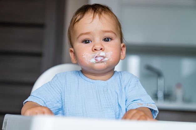 Baby isst Essen in der Küche Füttern von Babynahrung für Baby Schmutziges lustiges Kind isst Brei auf dem Stuhl