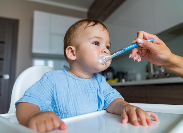 Baby isst Essen in der Küche Mutter füttert Baby mit Löffel drinnen