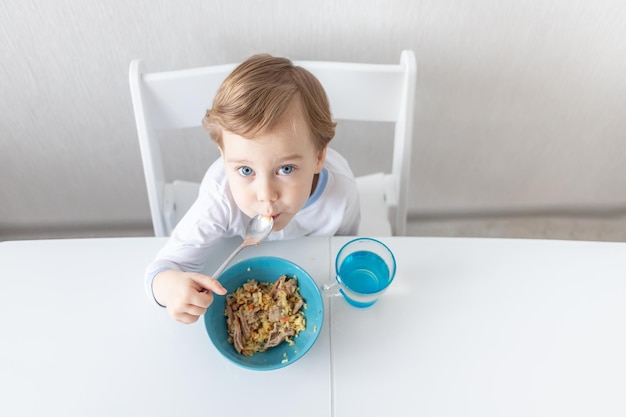 Baby isst mit einem Löffel zu Hause das Konzept von Nahrung und Ernährung für Kinder