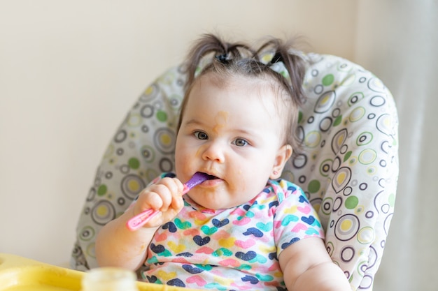 Baby isst sich mit einem Löffel Kartoffelpüree aus einem Glas, dem Konzept der Babynahrung