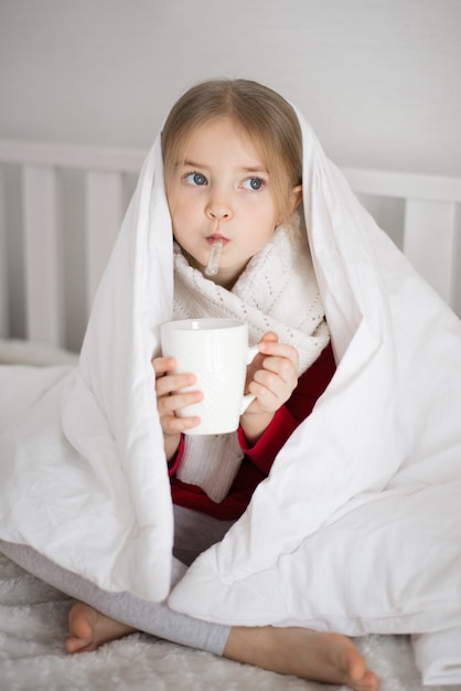 Baby ist krank, hält ein Thermometer in der Hand, unter der Decke, Augen traurig, Virus