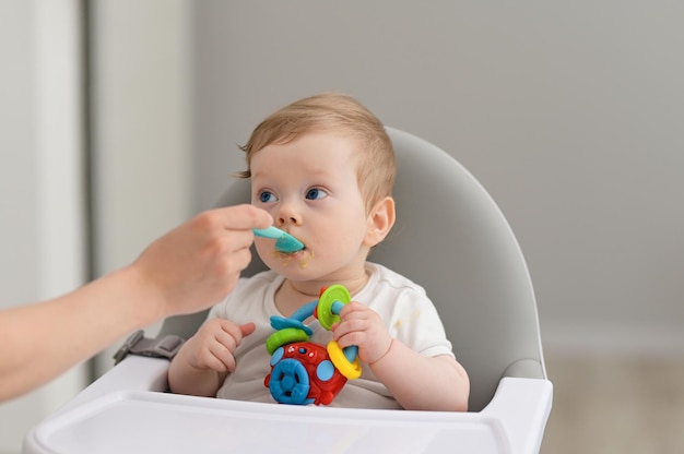 Baby Junge isst Mischung pürierte Nahrung sitzt auf Hochstuhl Mutter füttert Kind