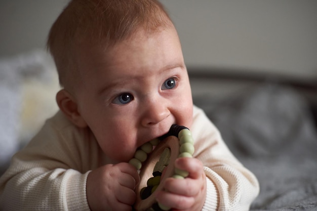 Baby kaut Beißring Spielzeug Säugling wächst ersten Zahn Junge beißt Spielzeug auf Elternbett Hübscher sechsmonatiger alter Junge Realistisches Kleinkind-Home-Porträt