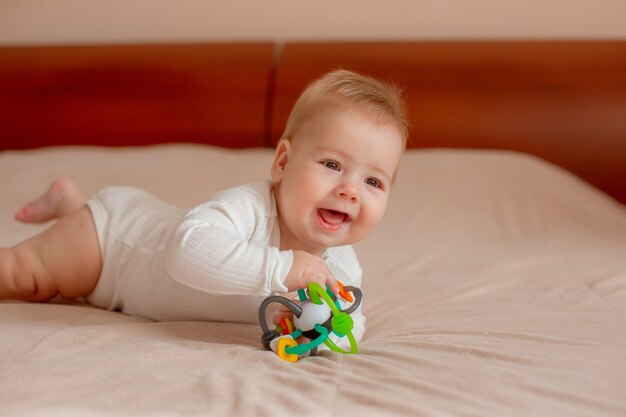 Baby liegt auf dem Bauch mit einem Spielzeug auf dem Bett im Schlafzimmer