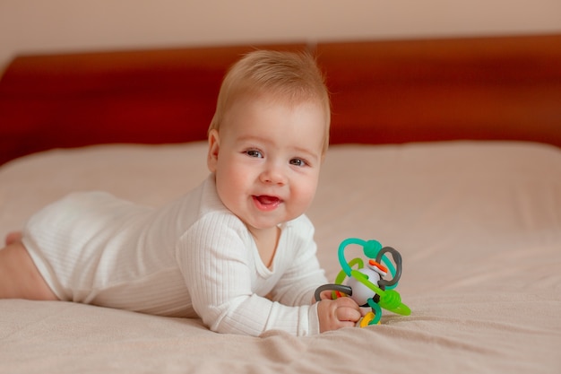 Baby liegt auf dem Bauch mit einem Spielzeug auf dem Bett im Schlafzimmer