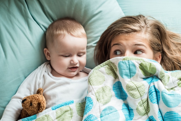 Baby liegt mit seiner Schwester im Bett