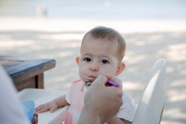 Baby Mädchen isst Brei Papa füttert kleine Tochter mit einem Löffel gegen tropischen Strand