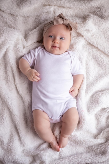 Baby Mädchen liegt auf einer weißen Decke in weißen Kleidern auf dem Bauch und lächelt in die Kamera Baby Morgen Baby Stuff Konzept